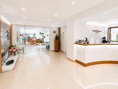 Helle Hotellobby mit Empfangstresen, Sitzbereich und Zugang zu einem Restaurant.