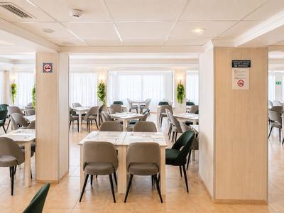 Innenansicht eines modernen Hotelrestaurants mit Tischen, Stühlen und Tageslicht.