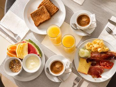 Frühstückstisch mit Eiern, Speck, Toast, Kaffee und Orangensaft in weißem Geschirr.