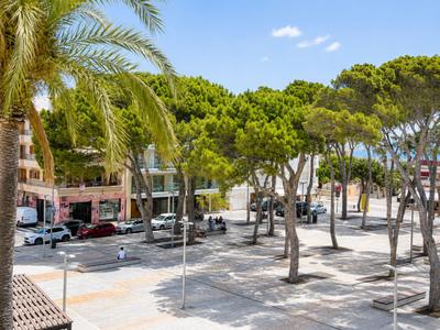 Eine baumbestandene, gepflasterte Plaza mit Parkplätzen in einem städtischen Urlaubsgebiet.
