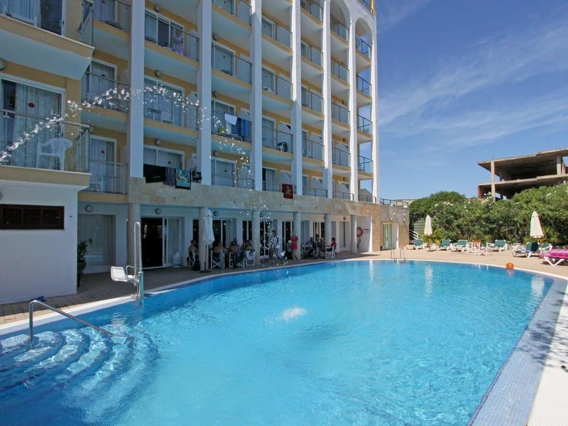 Piscina all'aperto accanto a un edificio alberghiero su più piani in una giornata di sole.