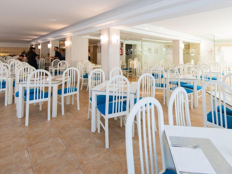 Grande sala da pranzo con sedie bianche e tovagliette blu in un hotel.