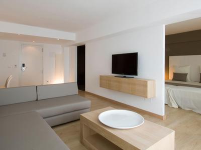 Helles Wohnzimmer mit grauem Ecksofa, Holztisch, Wand-TV und Blick ins Schlafzimmer.