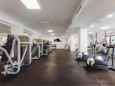 Moderner Fitnessraum mit Cardiogeräten, Kraftmaschinen und großem, dunklem Gummiboden.