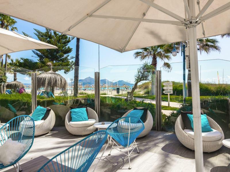 Taras z nowoczesnymi miejscami do siedzenia i parasolem, palmy i widok na góry w tle.