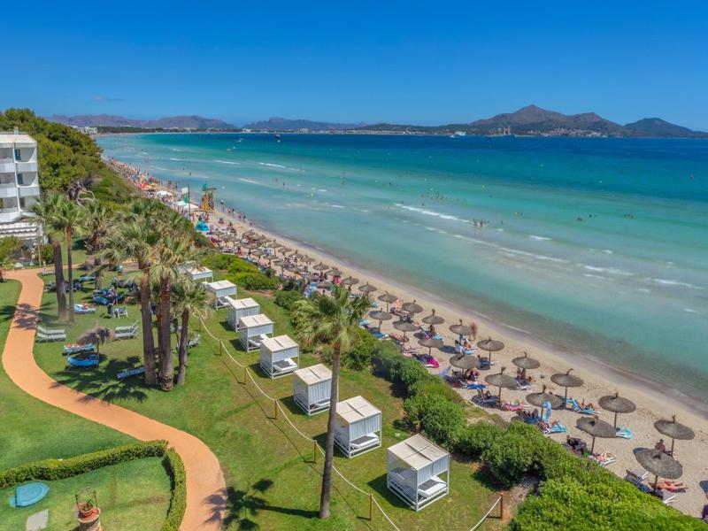 Długa piaszczysta plaża z leżakami, palmami i hotelami wzdłuż wybrzeża pod czystym niebem.