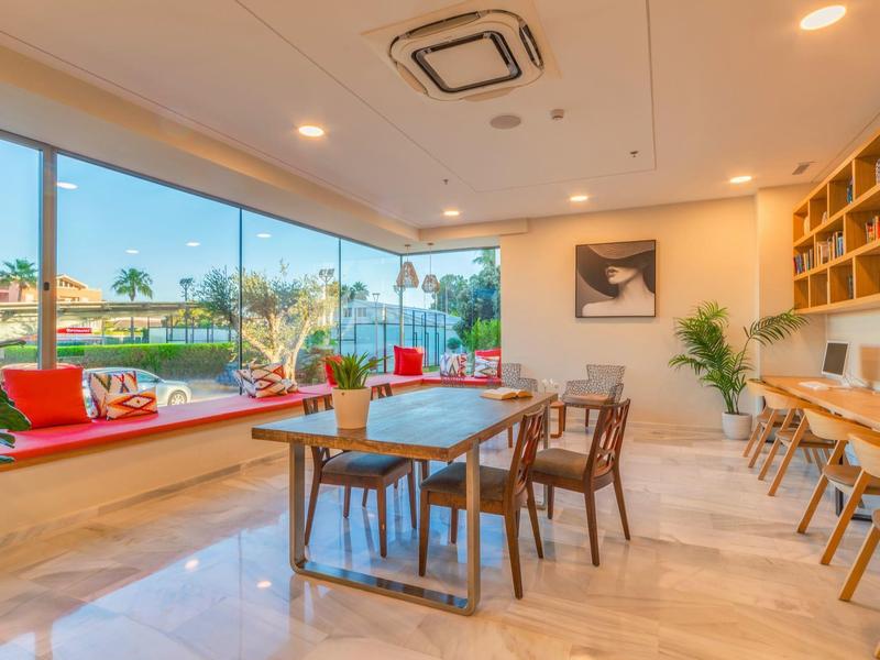 Jasny, nowoczesny salon hotelowy z wygodnymi krzesłami, stołami i dużymi oknami.