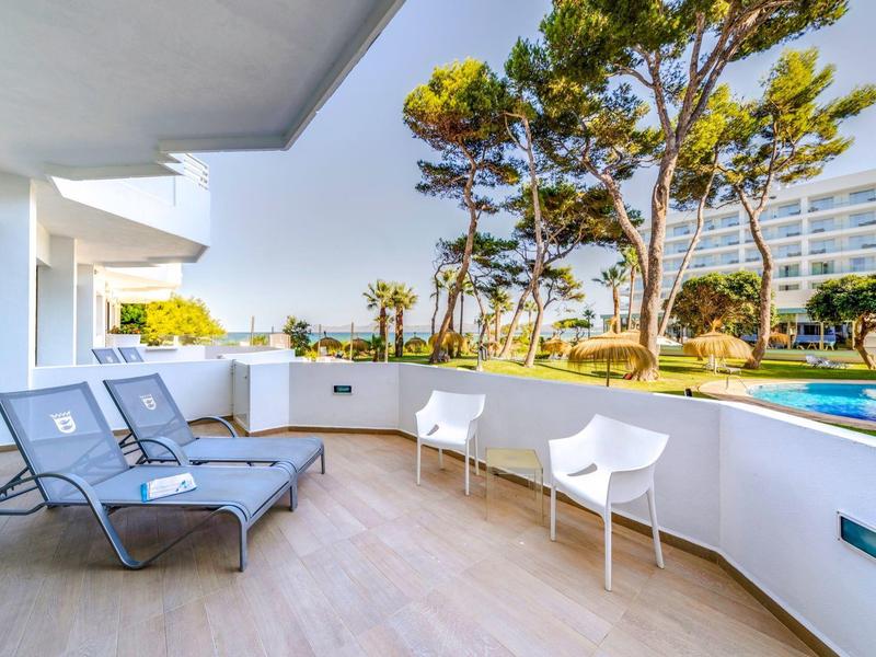 Balkon z leżakami i krzesłami obok basenu z widokiem na drzewa i budynki hotelowe.