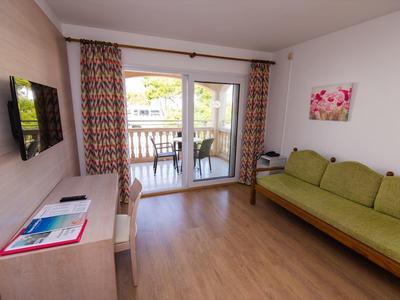 Wohnzimmer mit grünem Sofa, Schreibtisch, Fernseher und Balkon mit Aussicht.