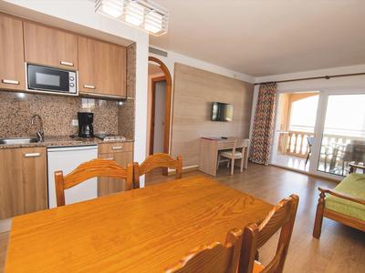 Moderner Wohnbereich mit Küchenzeile, Holztisch, Stühlen und Balkon mit Meerblick