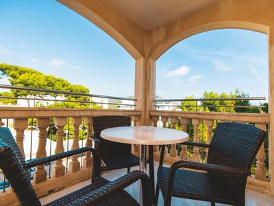 Balkon mit einem runden weißen Tisch und vier schwarzen Stühlen, Blick auf Bäume und blauen Himmel.
