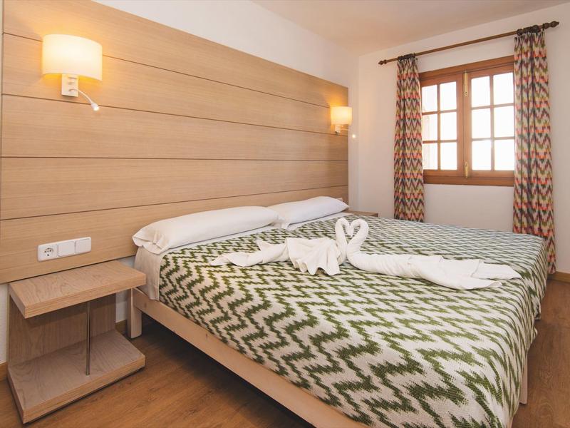 Gemütliches Hotelzimmer mit Doppelbett, Holzverkleidung und Fenster mit gemusterten Vorhängen.
