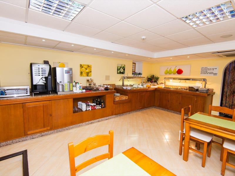 Helles Frühstückszimmer mit Buffet, Kaffeemaschine und mehreren Holztischen und Stühlen.