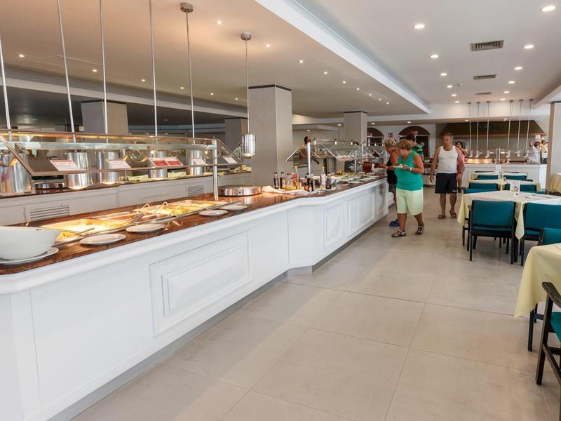 Jasna hotelowa strefa bufetu z białymi ladami, podgrzewaczami jedzenia i stołami z gośćmi.