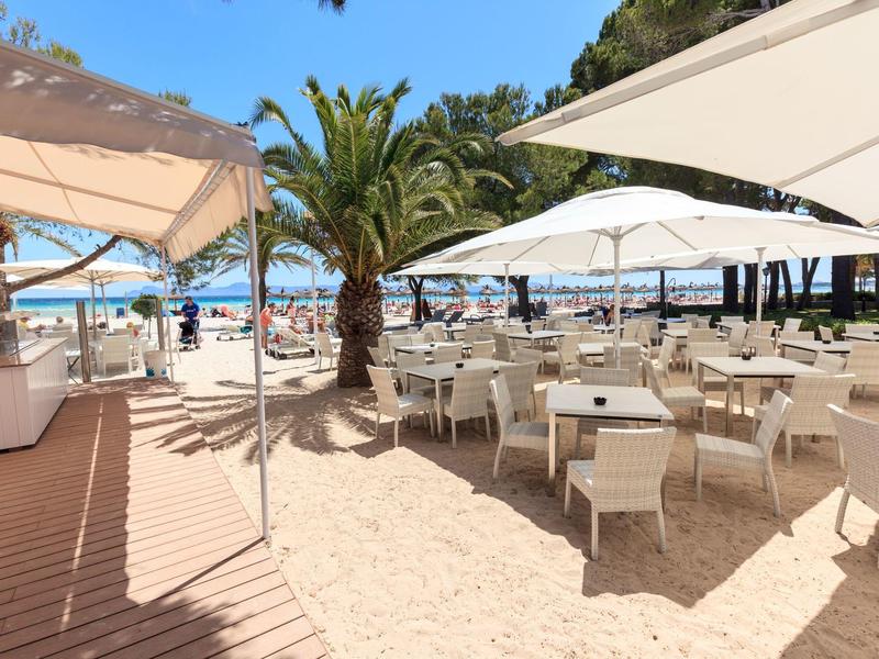 Restauracja przy plaży z białymi stołami, krzesłami, parasolami, palmami i widokiem na ocean