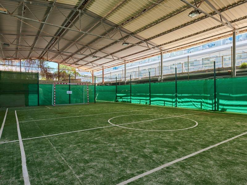 Kryte małe boisko do piłki nożnej ze sztuczną trawą i zielonym ogrodzeniem wewnątrz budynku