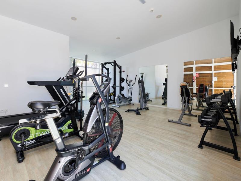 Nowoczesna siłownia z rowerami stacjonarnymi, maszynami do ćwiczeń i ławkami w jasnym pomieszczeniu.