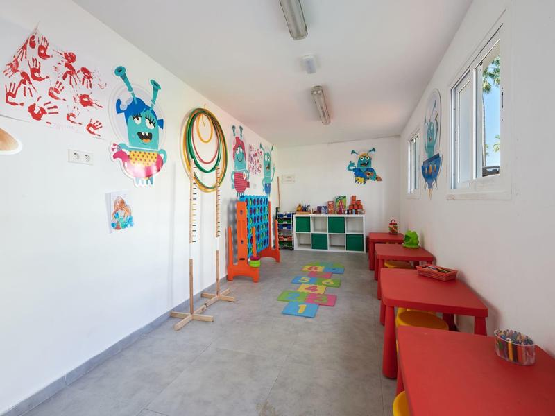 Jasny pokój zabaw z kolorowymi malowidłami na ścianach, czerwonymi stołami, krzesłami i zabawkami dla dzieci.