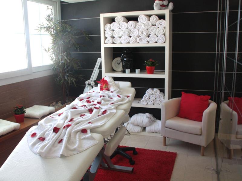 Hell eingerichteter Massage- oder Behandlungsraum mit Liege, weißen Handtüchern und roter Deko.