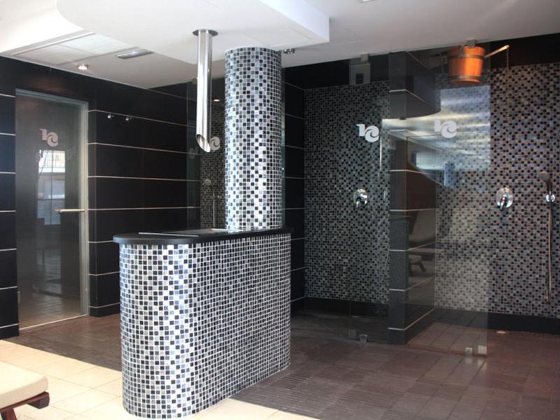 Modernes Badezimmer mit hellen Fliesen, beleuchtetem Spiegel, Waschbecken und begehbarer Dusche.