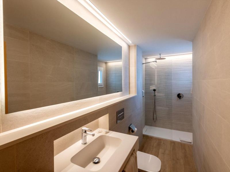 Modernes Badezimmer mit hellen Fliesen, beleuchtetem Spiegel, Waschbecken und begehbarer Dusche.