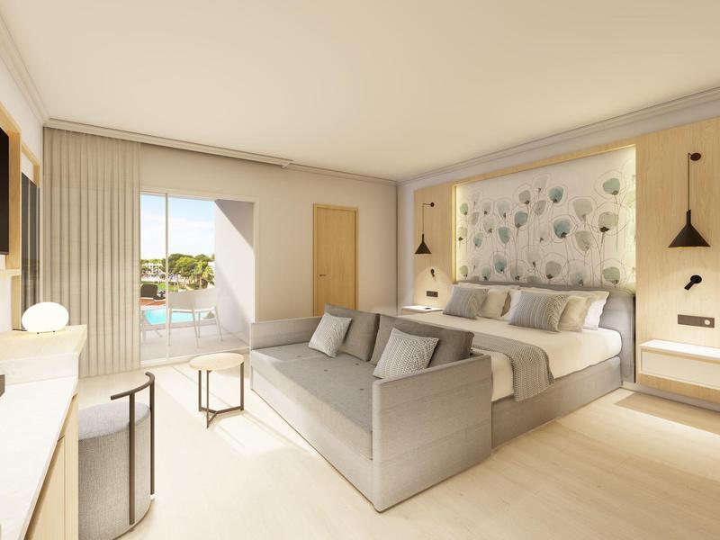 Helles Hotelzimmer mit Doppelbett, grauem Sofa, Holzmöbeln und Balkon mit Blick ins Grüne.