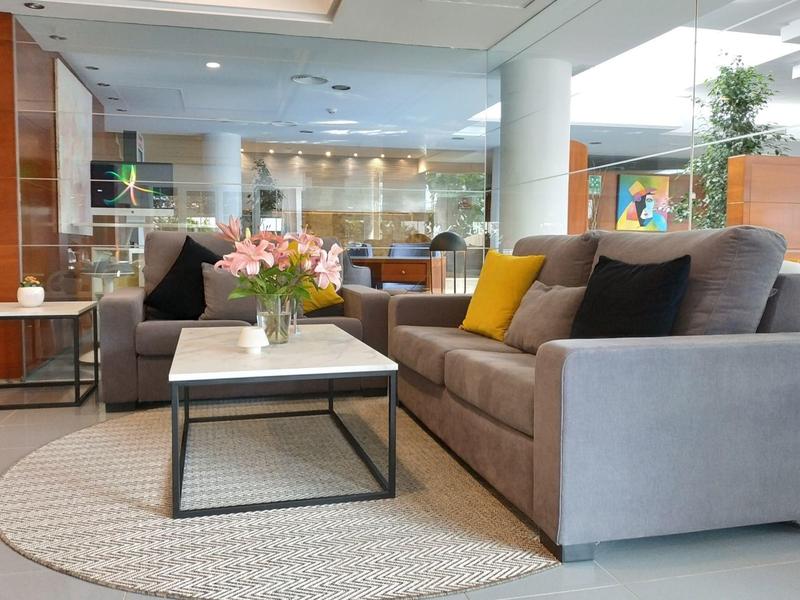 Moderner Wohnraum mit grauem Sofa, bunten Kissen, rechteckigem Tisch und rundem Teppich.