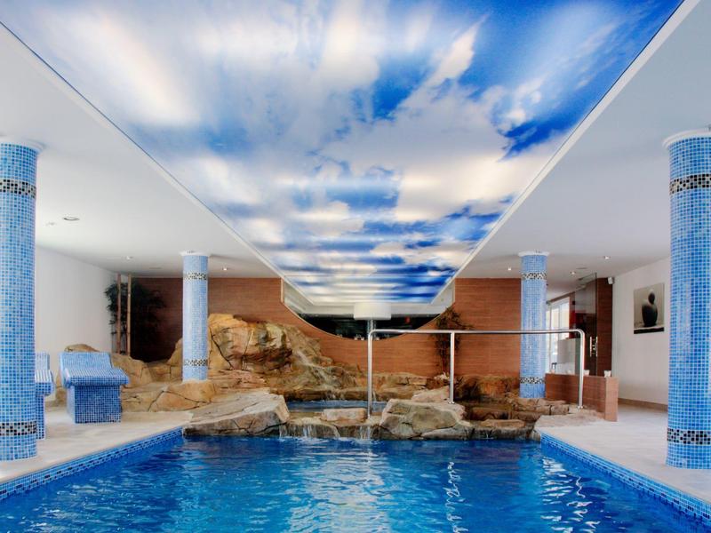 Innenpool mit blauer Wasserfläche, Säulen mit Muster und Himmelmotiv an der Decke.