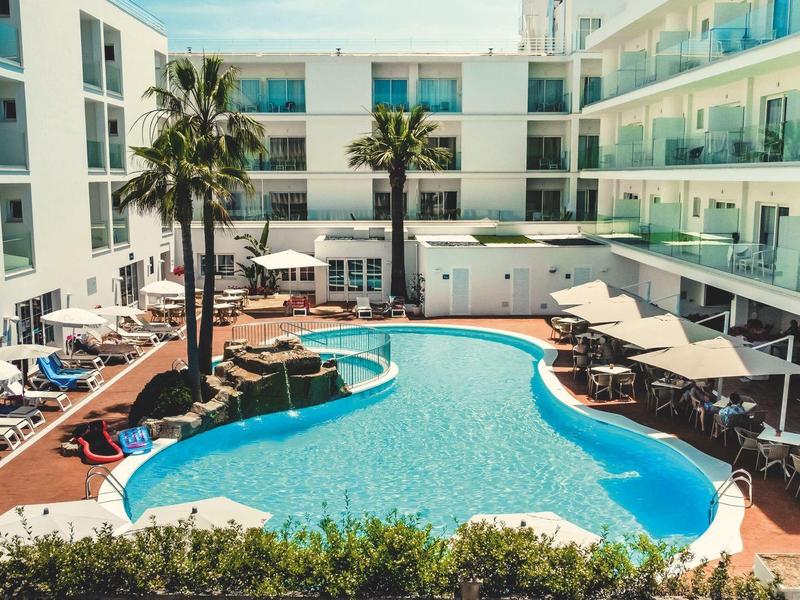 Moderner Hotelinnenhof mit geschwungenem Pool, Palmen, Sonnenschirmen und Poolliegen.