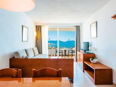 Světý obývací pokoj s pohovkou, TV a výhledem na moře přes balkonové dveře.