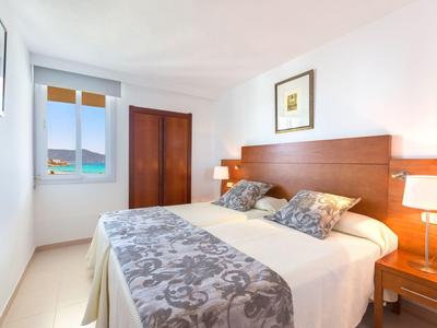 Světý hotelový pokoj s manželskou postelí, oknem s výhledem na moře a jednoduchým zařízením.