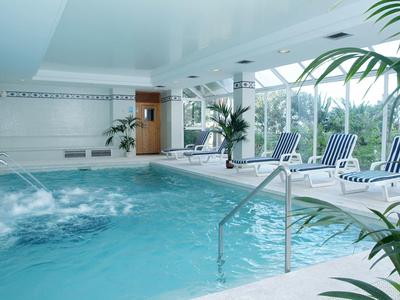 Vnitřní hotelový bazén s modrými lehátky a zelenými rostlinami.