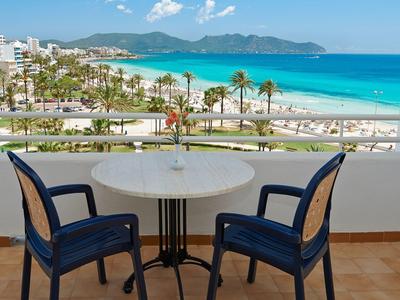 Stůl a židle na balkóně s výhledem na pláž a tyrkysové moře.