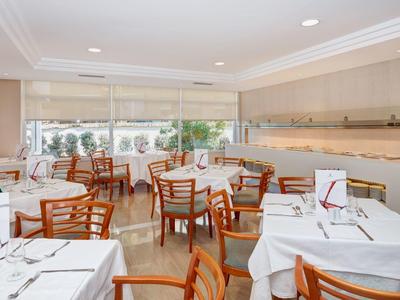 Světla jídelna s dřevěnými stoly a bílými ubrusy, pohled ven.