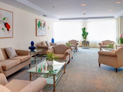 Světlý obývací pokoj s béžovými pohovkami, skleněnými stolky a moderními obrazy na stěnách.