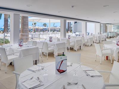 Prostorná světlá restaurace s velkými okny s výhledem na marinu a elegantně prostřené stoly.