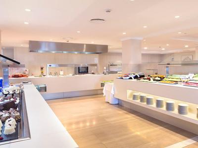 Světle moderní samoobslužná restaurace s různorodým bufetem a dřevěnou podlahou.