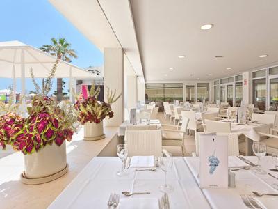 Hell eingerichtetes Restaurant mit Blumen auf den Tischen und Sicht nach draußen mit Sonnenschirmen.