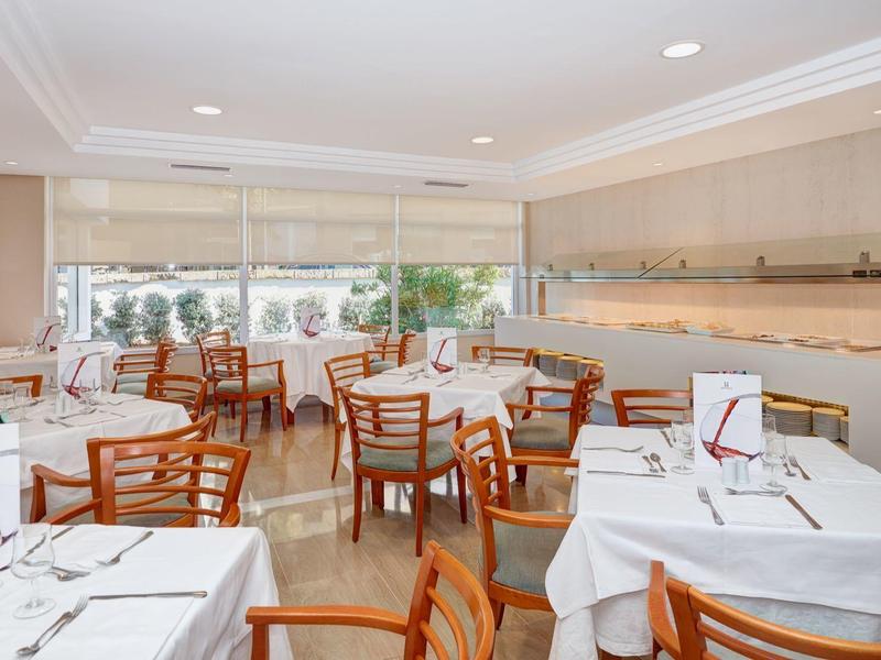 Světla jídelna s dřevěnými stoly a bílými ubrusy, pohled ven.