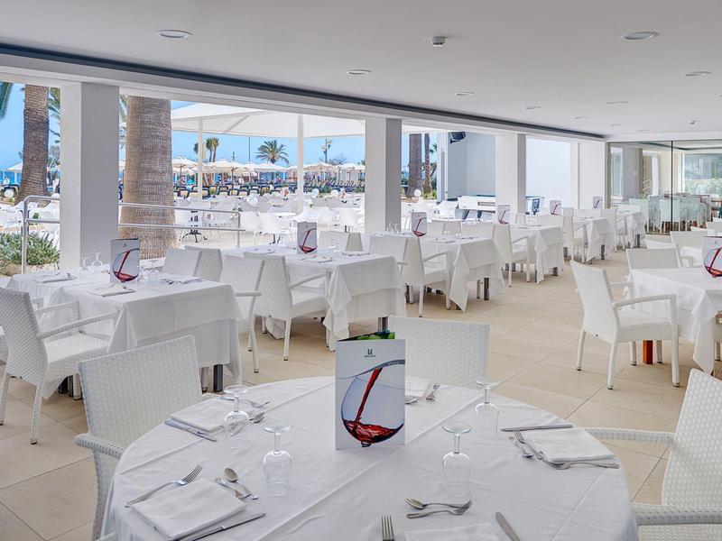 Prostorná světlá restaurace s velkými okny s výhledem na marinu a elegantně prostřené stoly.