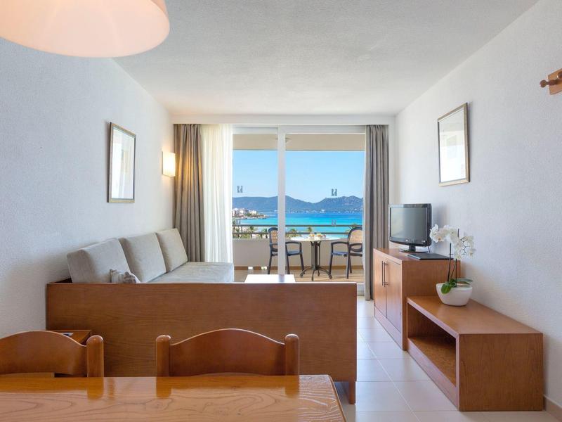 Světý obývací pokoj s pohovkou, stolem, televizí a výhledem na moře z balkonu.