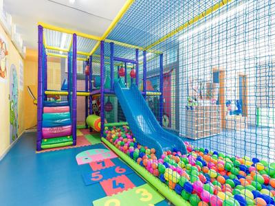 Kleurrijke kinderspeelruimte met glijbaan en ballenbak in een lichte kamer.