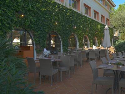 Buitenterras van een restaurant met een met klimop bedekte muur en tafels met stoelen onder een blauwe lucht.