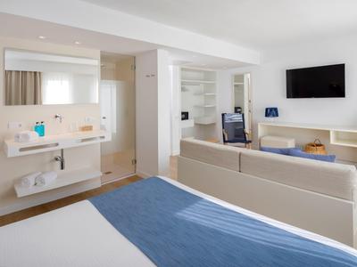 Modern hotelkamer met blauw bed, bank, tv en open badkamer.