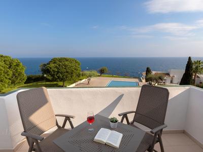 Terras met stoelen, tafel, open boek en glas met uitzicht op zee en blauwe lucht.