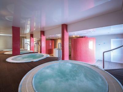Moderne wellnessruimte met twee ronde jacuzzi's en rode zuilen.