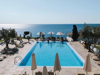 Sfeervol buitenzwembad met witte parasols en uitzicht op zee bij zonnig weer.
