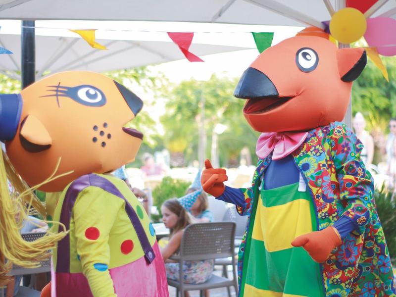 Twee kleurrijke mascottes met dierenhoofden bij een buitenactiviteit in een hotel.