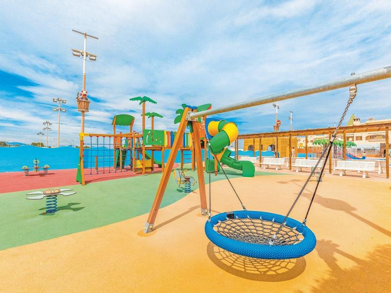 Kleurrijke speeltuin met schommels en klimtoestellen op hotelterrein.