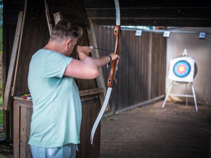 Man beoefent boogschieten binnenshuis gericht op een doelwit aan de muur.
